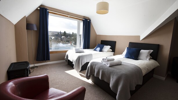 Habitación de hotel con dos camas, una silla roja, una lámpara y vistas al exterior.