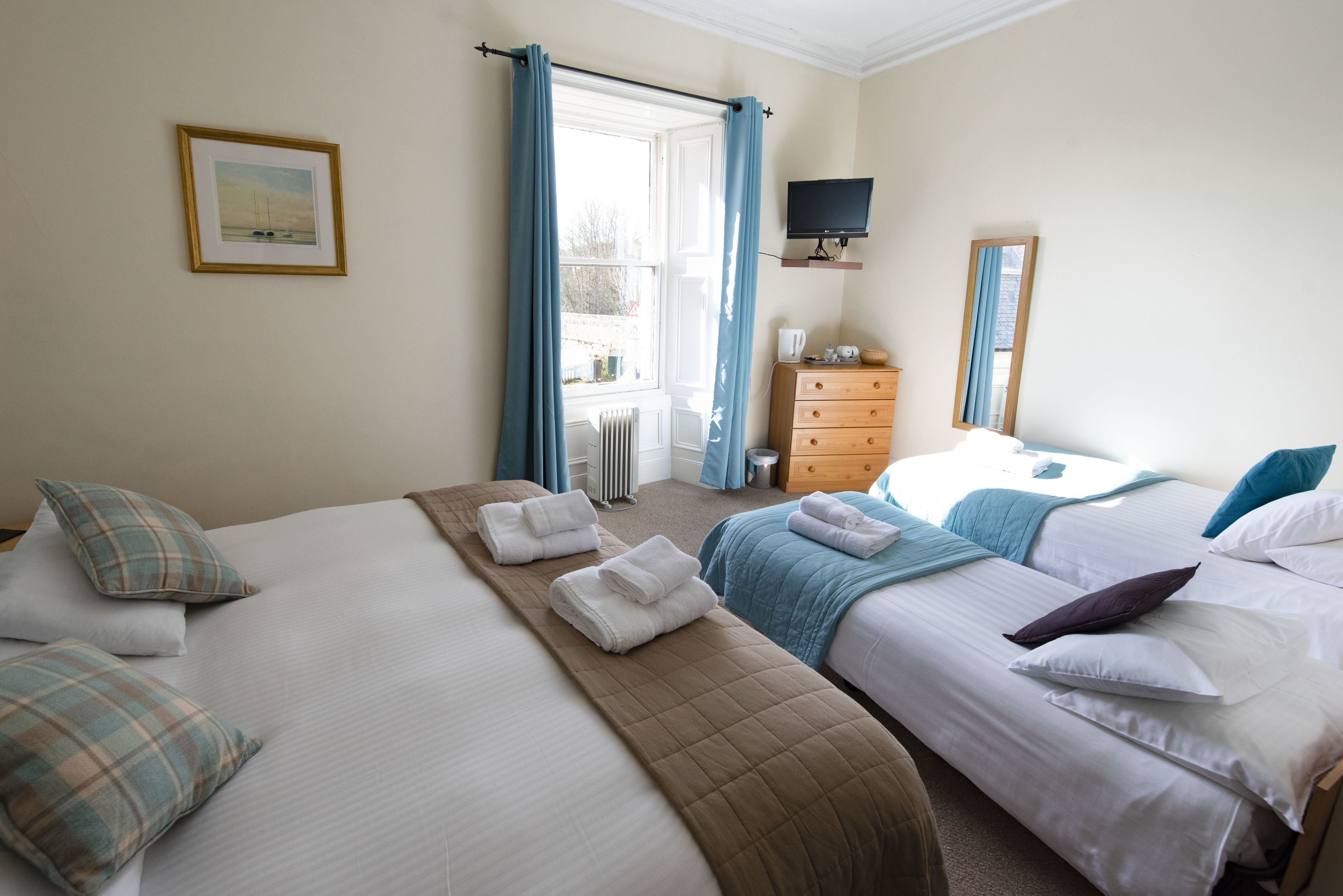 A hotel room with two beds, a dresser, a television, and a window with curtains.