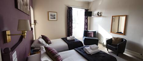 A hotel room with two beds, a desk, a chair, a TV, and a window with curtains.