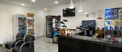 A reception area with a black counter, seating, a refrigerator, and a television.