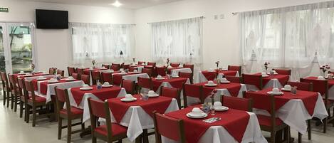 A dining area with multiple tables set for service, each with white tablecloths and red chair covers.