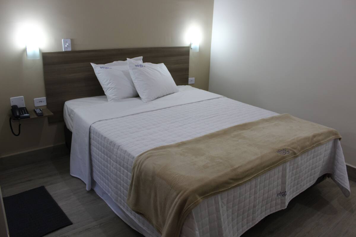 Une chambre d’hôtel équipée d’un lit, de tables de chevet, d’un téléphone et d’une lampe fixée au mur.