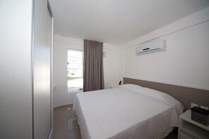 Una habitación de hotel con una cama, una mesita de noche, un equipo de aire acondicionado y una ventana con cortinas.