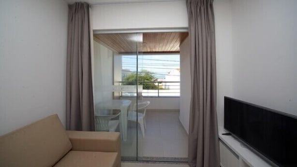 A balcony with a sofa, a glass door, and a TV. - Caravaggio Residence (Natal)