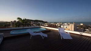 A wooden deck with a pool and lounge chairs overlooking a cityscape and the sea. - Caravaggio Residence (Natal)
