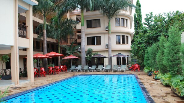 A swimming pool with lounge chairs and umbrellas, surrounded by palm trees and a multi-story building with balconies. - Parkview Inn (Moshi)