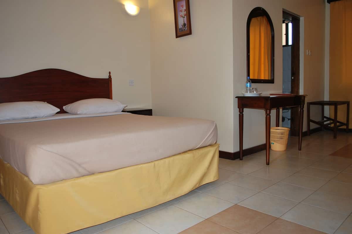 A hotel room with a bed, a desk, a chair, a mirror, and a door.