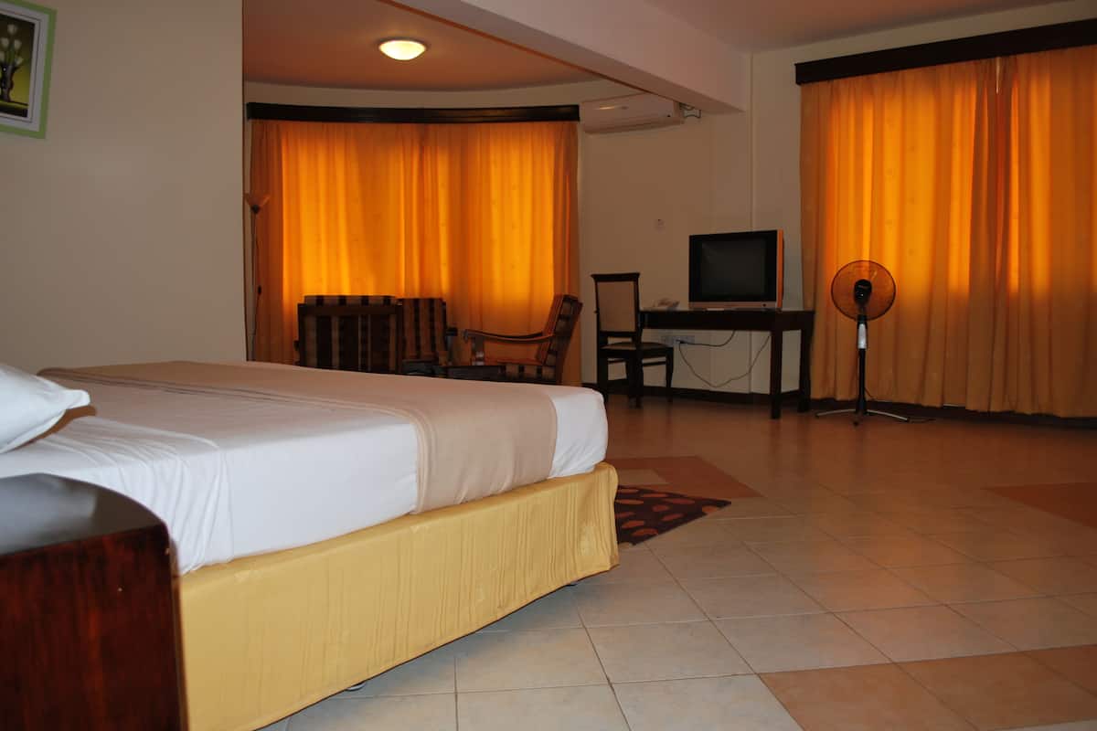 A hotel room with a bed, a desk with a computer, a chair, and a standing fan.