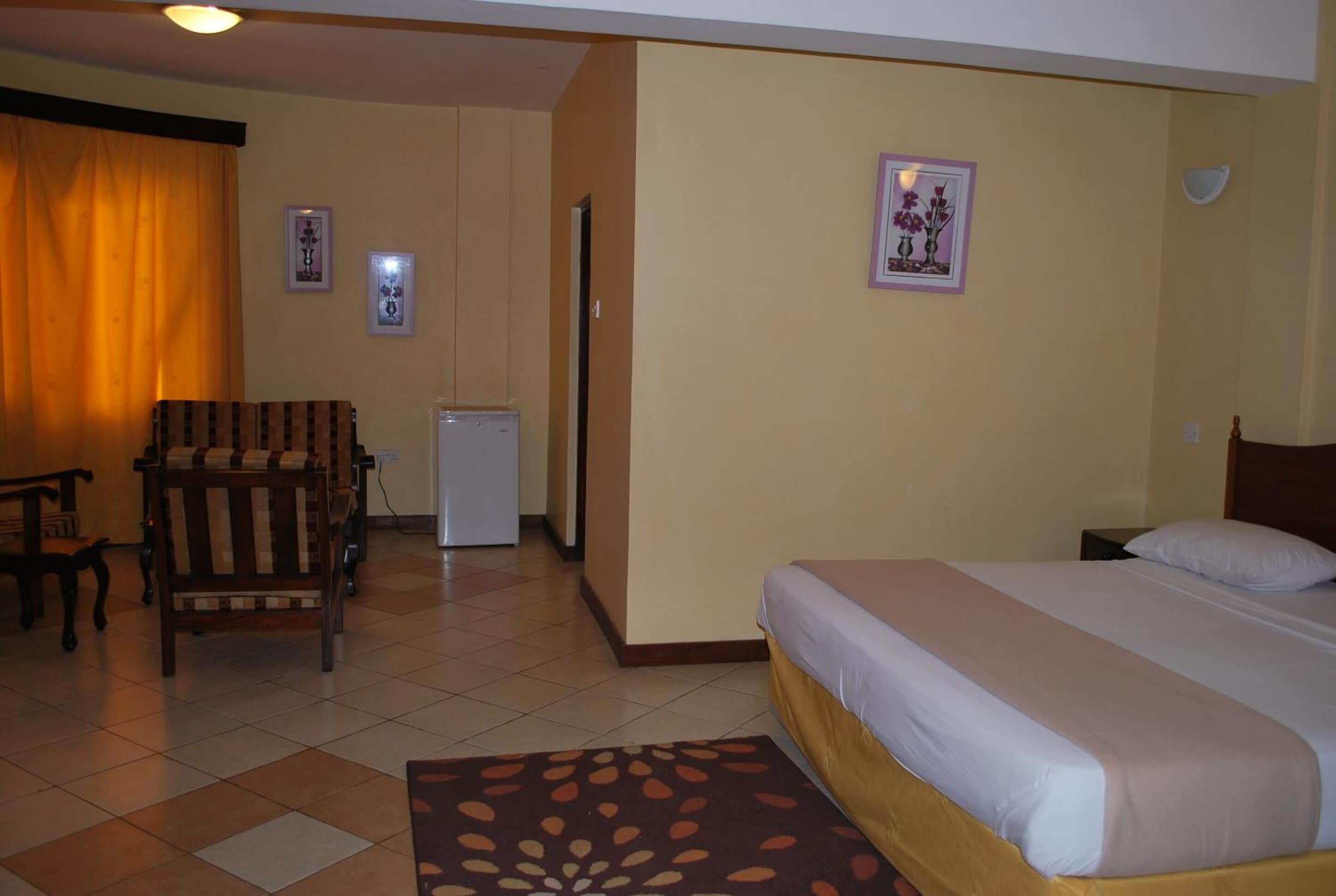 A hotel room with a bed, a chair, a desk, and a small refrigerator.