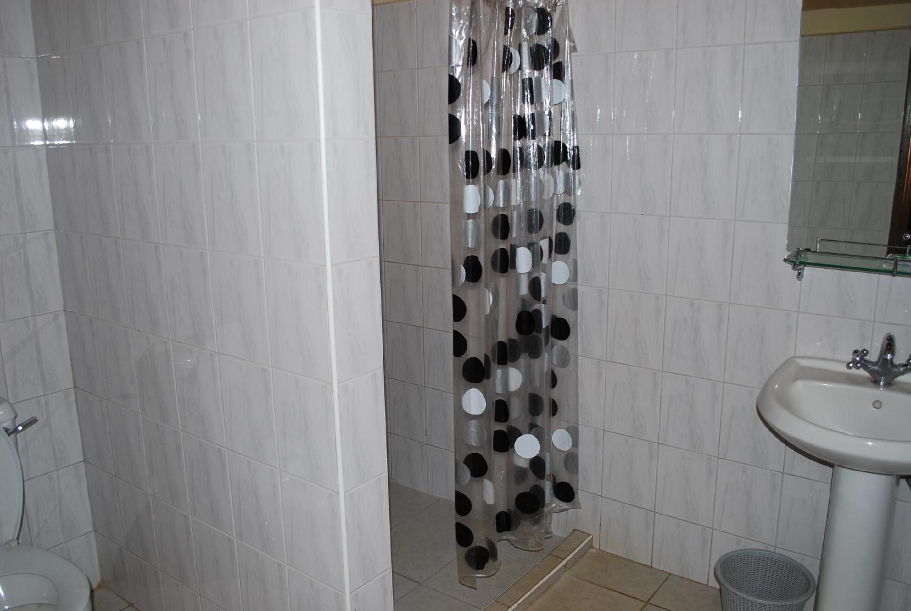 A bathroom with white tiled walls, a shower curtain with a polka dot pattern, a white sink, and a trash bin.