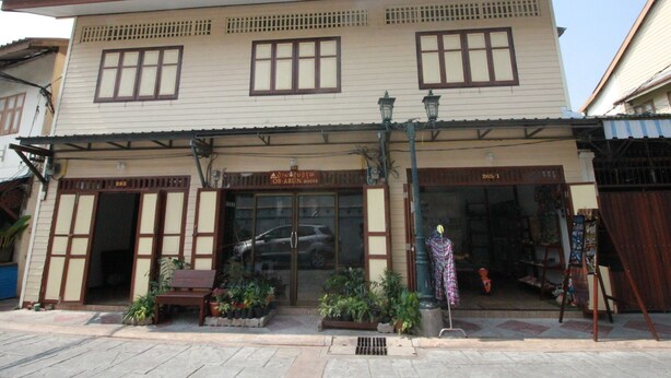 A two-story building with a traditional architectural style, featuring a large entrance with glass doors, potted plants, and a bench outside. - OB-ARUN House (Bangkok)