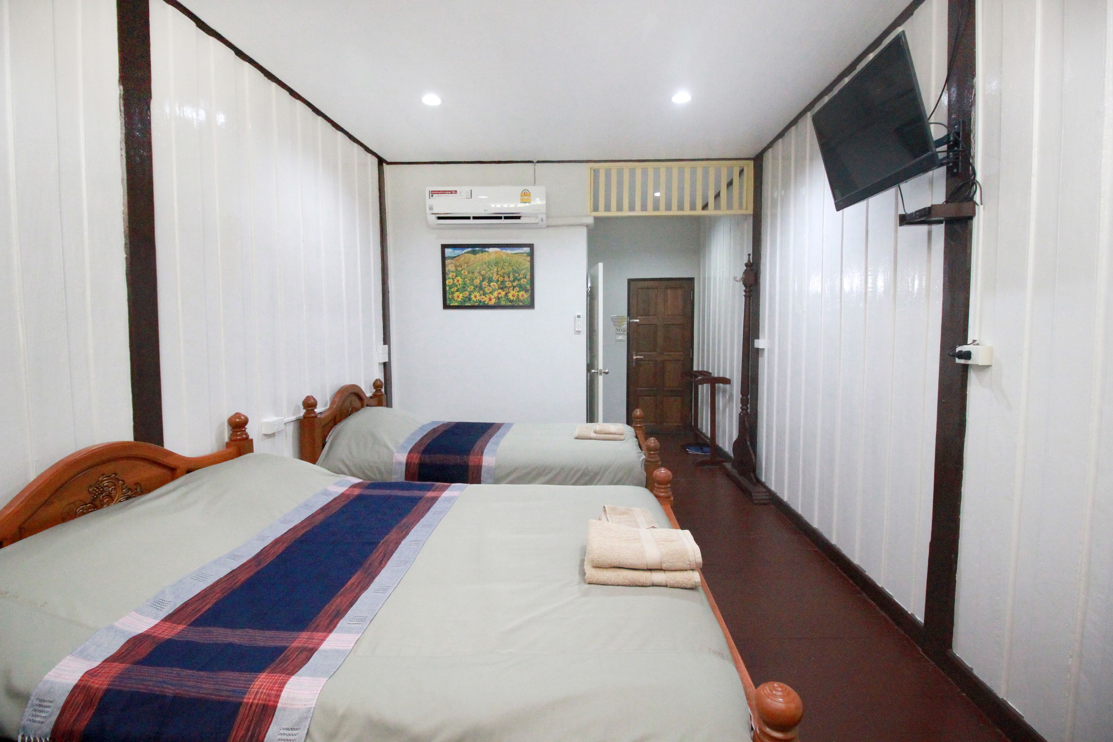 A hotel room with two beds, a television, an air conditioning unit, and a painting on the wall.