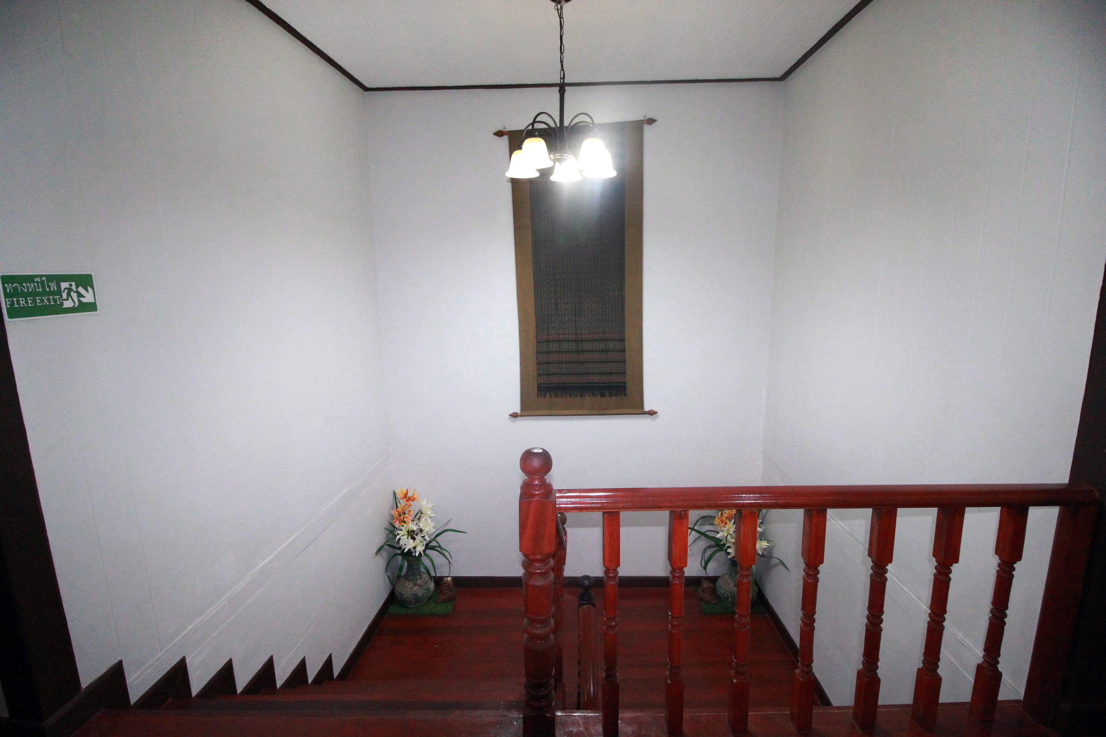 A staircase with a wooden handrail, a green emergency exit sign, and a window with a curtain.