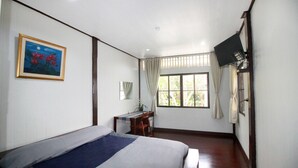 A bedroom with a bed, a desk, a chair, a TV, and a window with curtains. - OB-ARUN House (Bangkok)