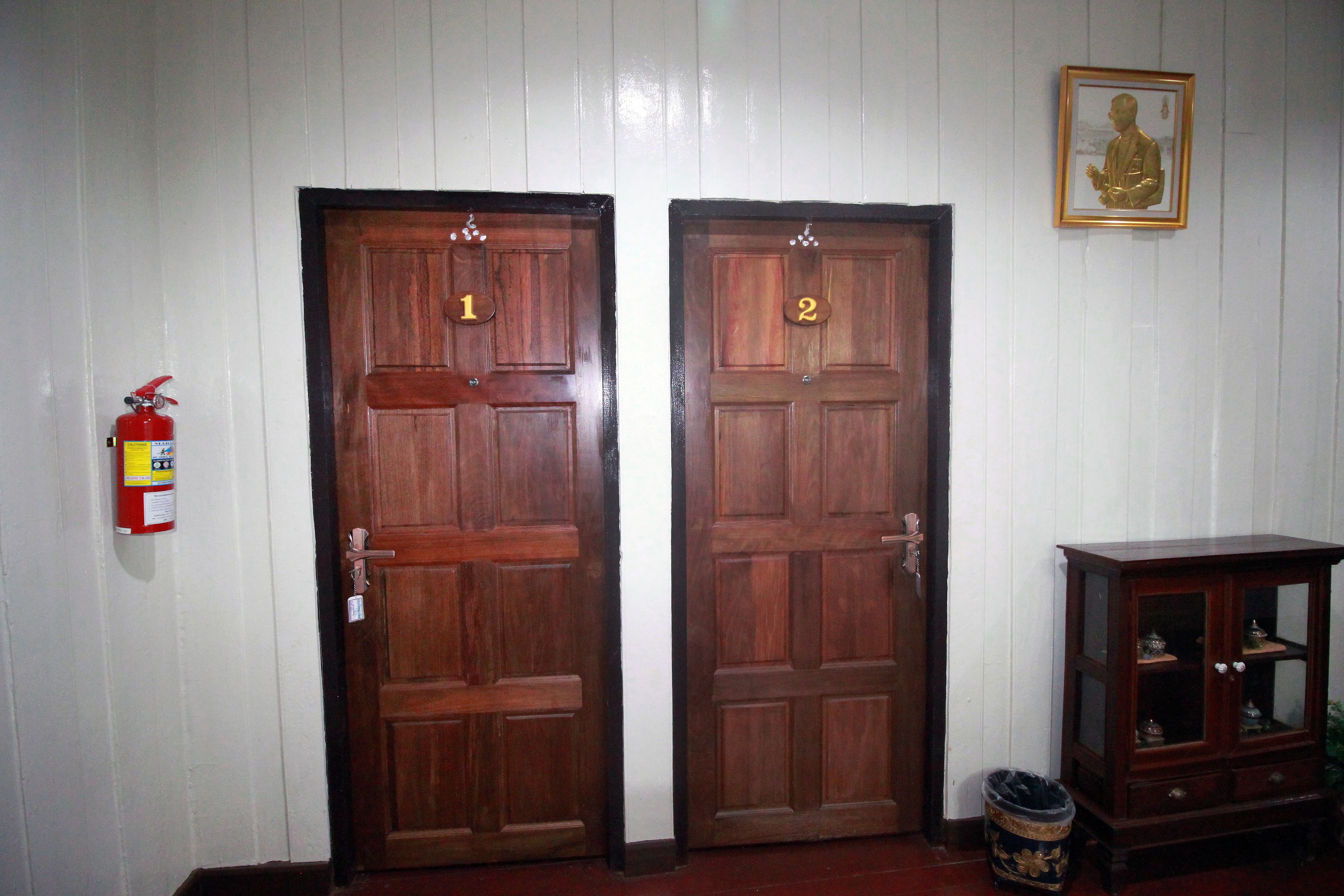 Zwei Holztüren mit den Nummern 1 und 2, ein Feuerlöscher und ein Schrank mit Glastüren.