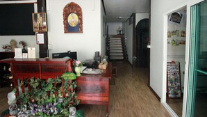 A reception desk with a wooden finish, a framed portrait above it, and a small desk lamp. There is a staircase leading to an upper level, and a bulletin board with various items on the right side. - OB-ARUN House (Bangkok)