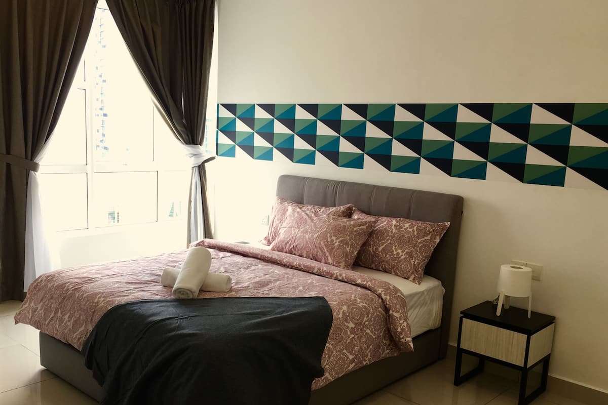 A bedroom with a bed, a nightstand, a patterned wall, and a window with curtains.