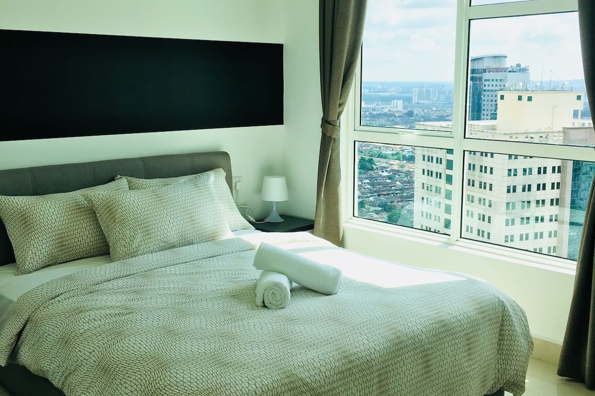 A hotel room with a large bed, a flat-screen TV mounted on the wall, a window with curtains, and a city view.
