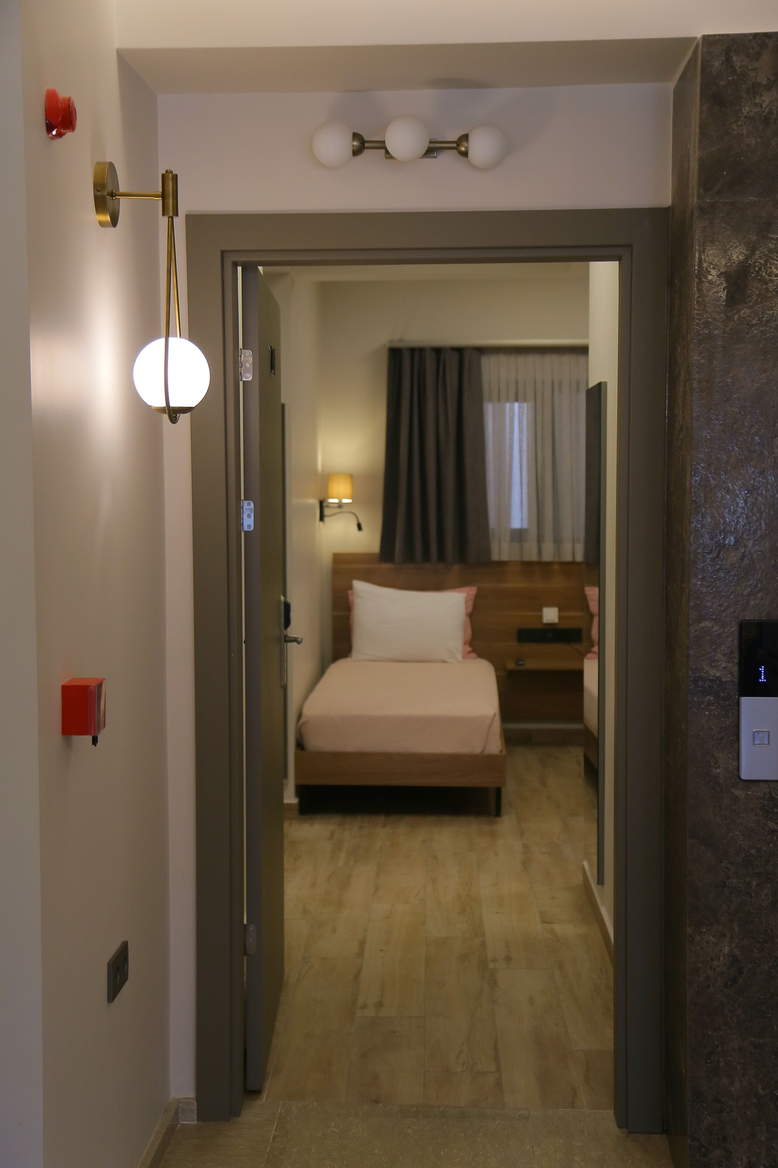Habitación de hotel con cama, mesita de noche, lámpara y vista a la habitación contigua.