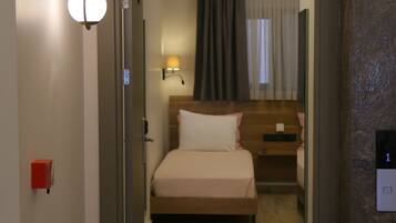 Habitación de hotel con cama, mesita de noche, lámpara y vista a la habitación contigua.