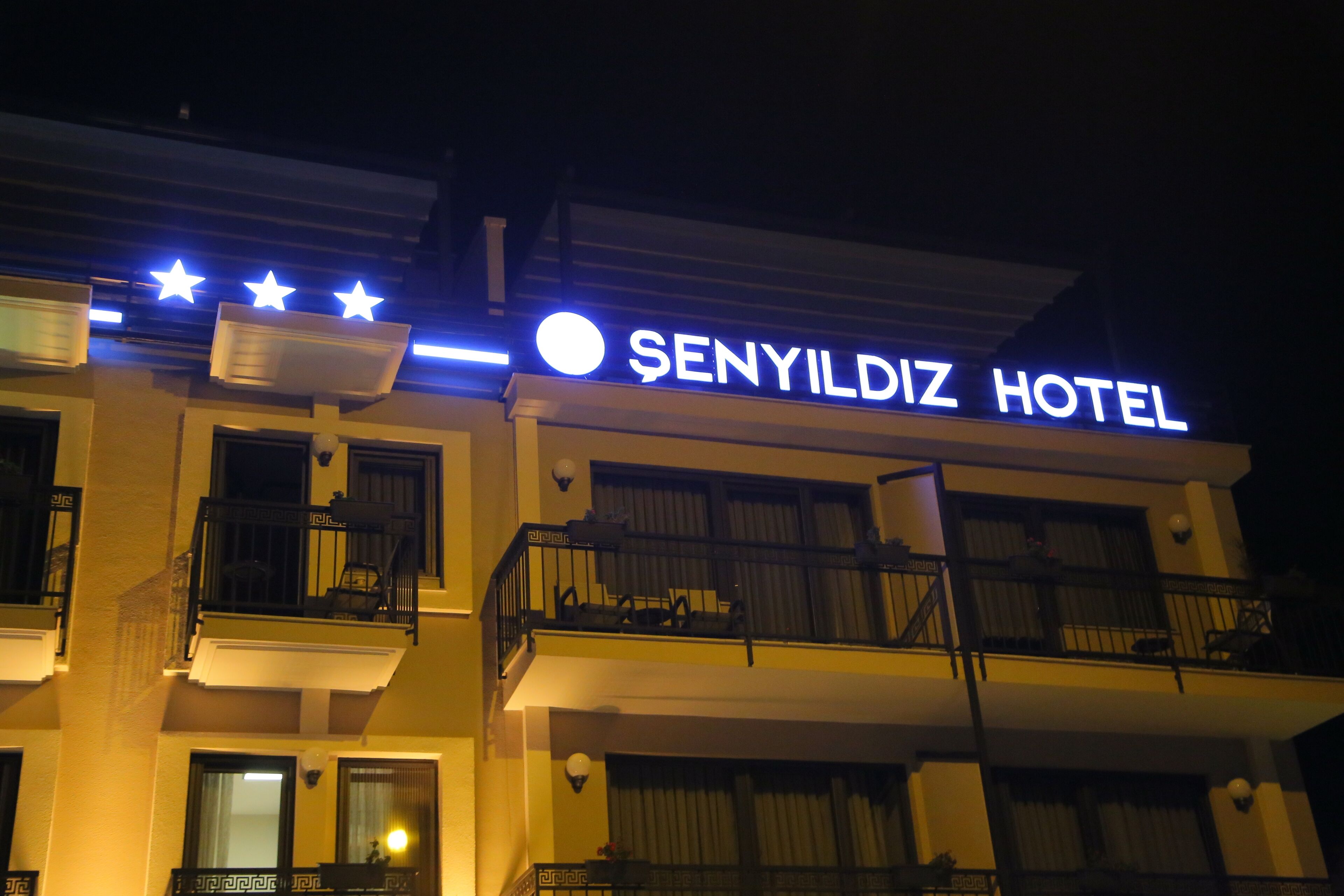 The exterior of the SenYildiz Hotel with illuminated signage, balconies, and windows.