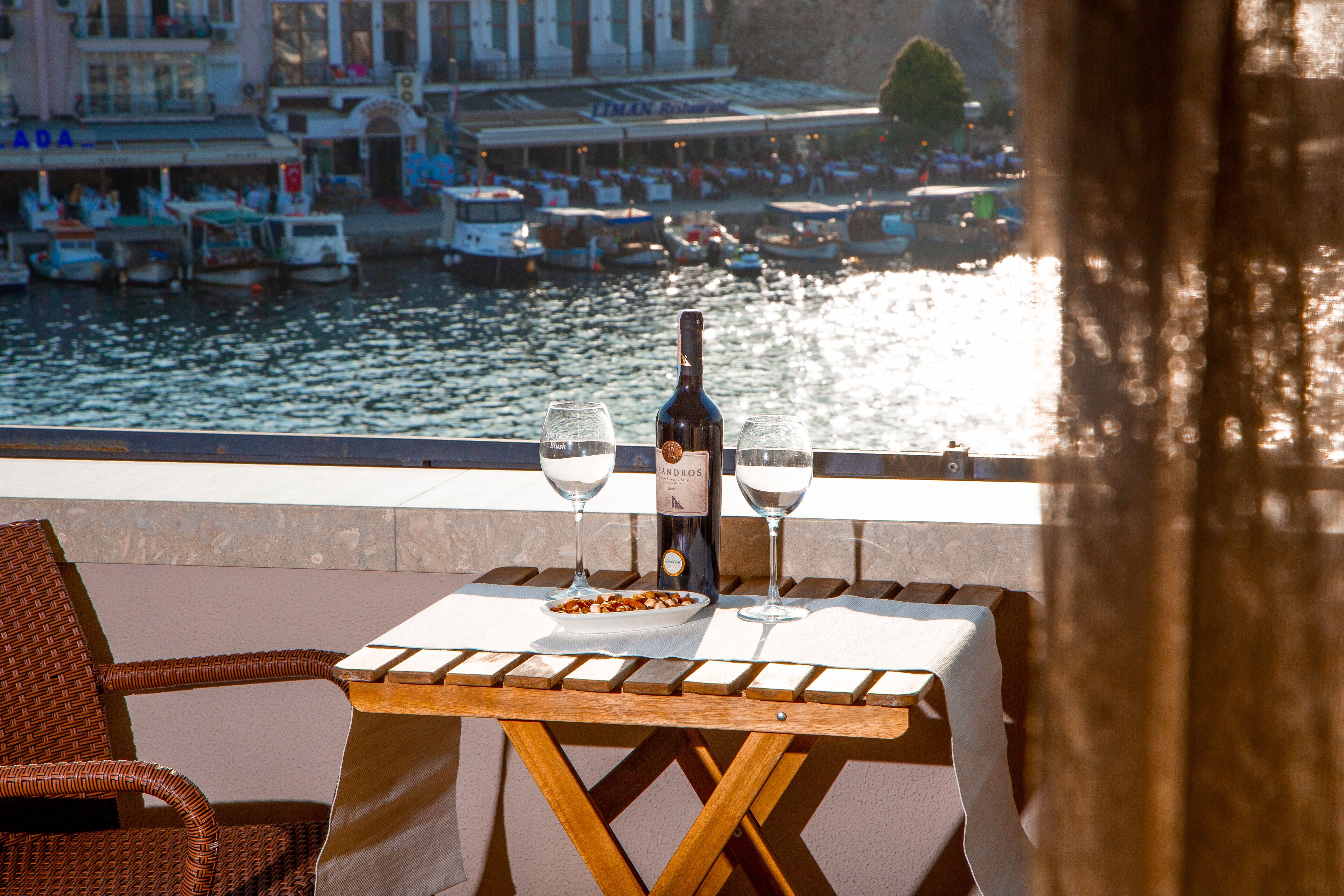 Una mesa con una botella de vino y dos copas, con vistas a un río y barcos.