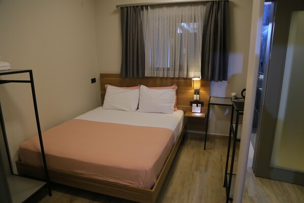 A hotel room with a bed, a nightstand, a lamp, and a window with curtains.