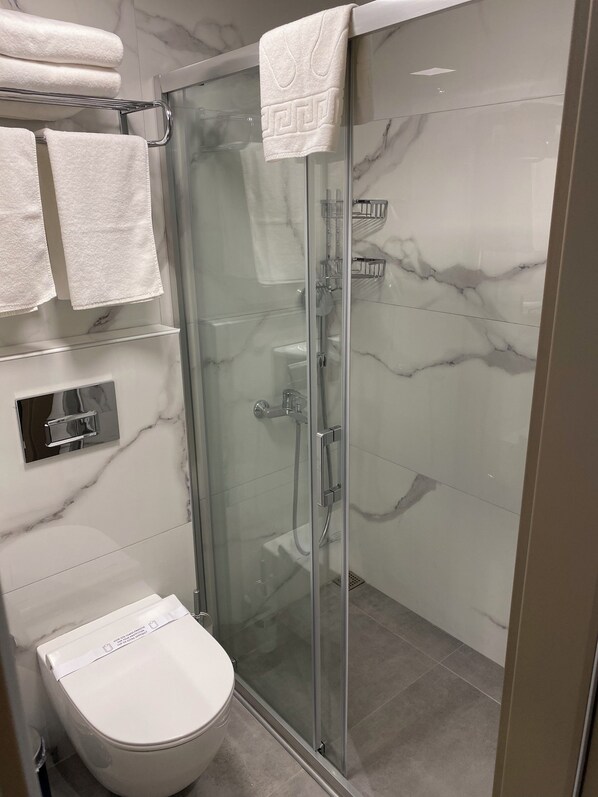 Et moderne badeværelse med en glasafskærmet bruseniche, toilet og en marmorbeklædt bagvæg.