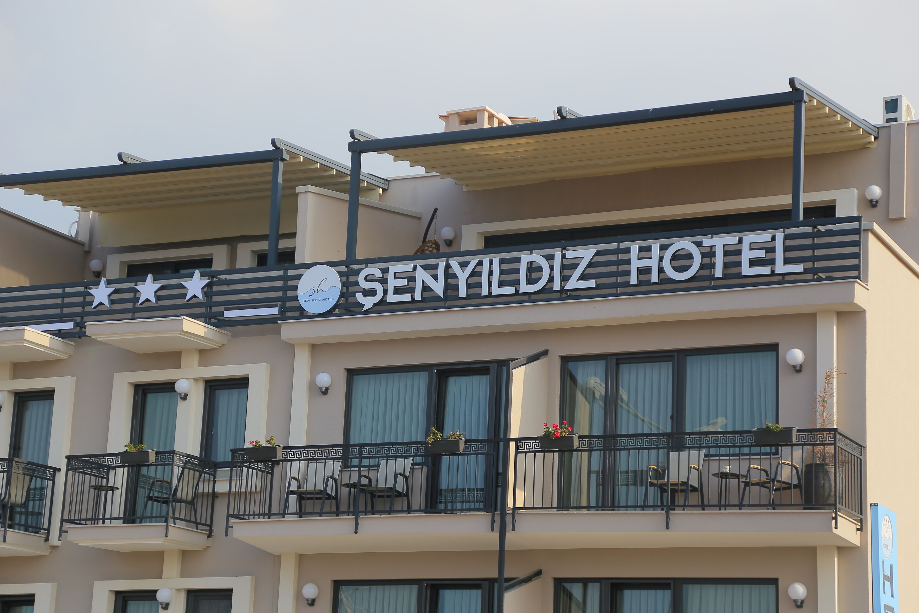 A hotel with balconies, outdoor seating, and a sign reading "SENYILDIZ HOTEL".