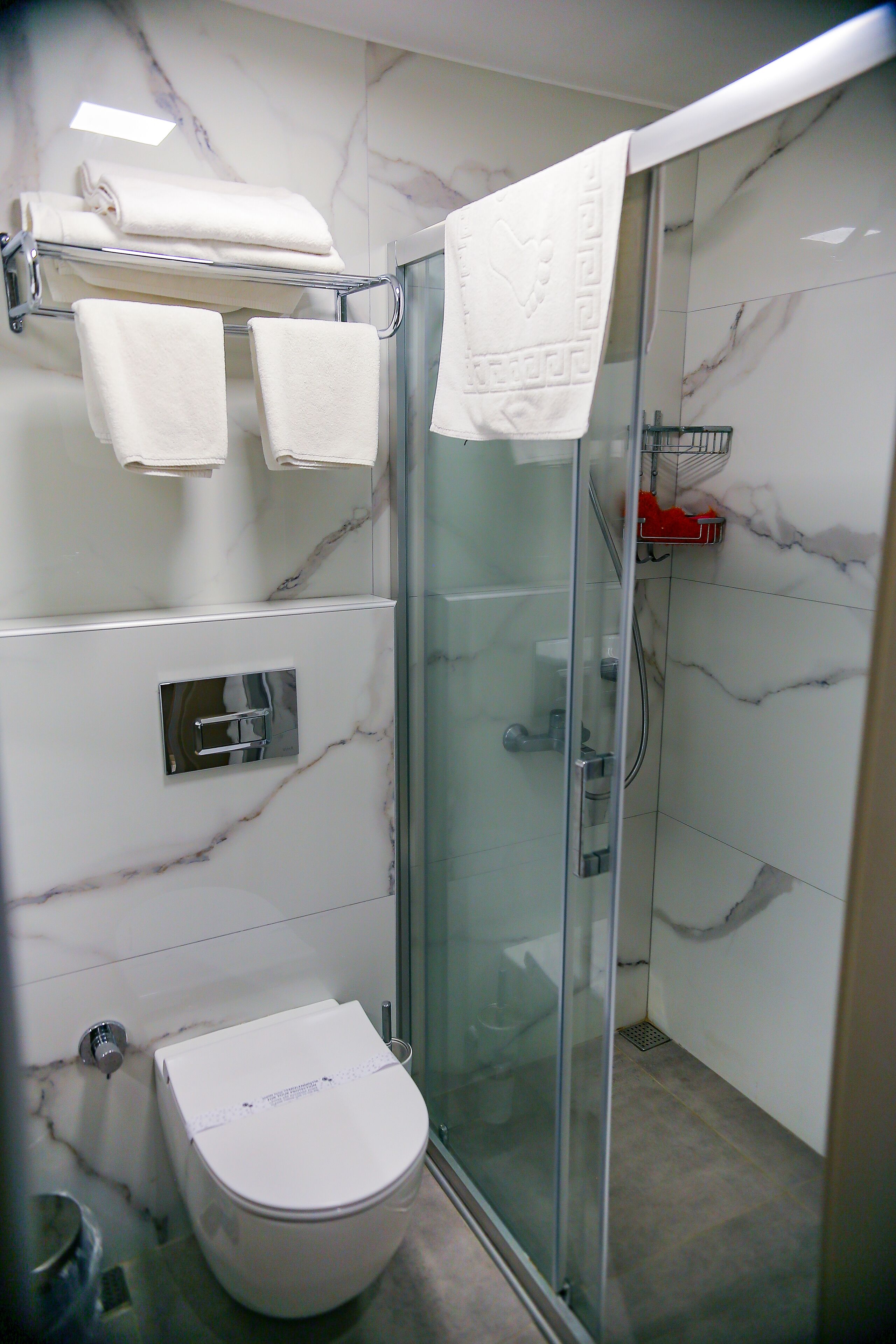 A bathroom with a glass-enclosed shower, a white toilet, and a marble backsplash.