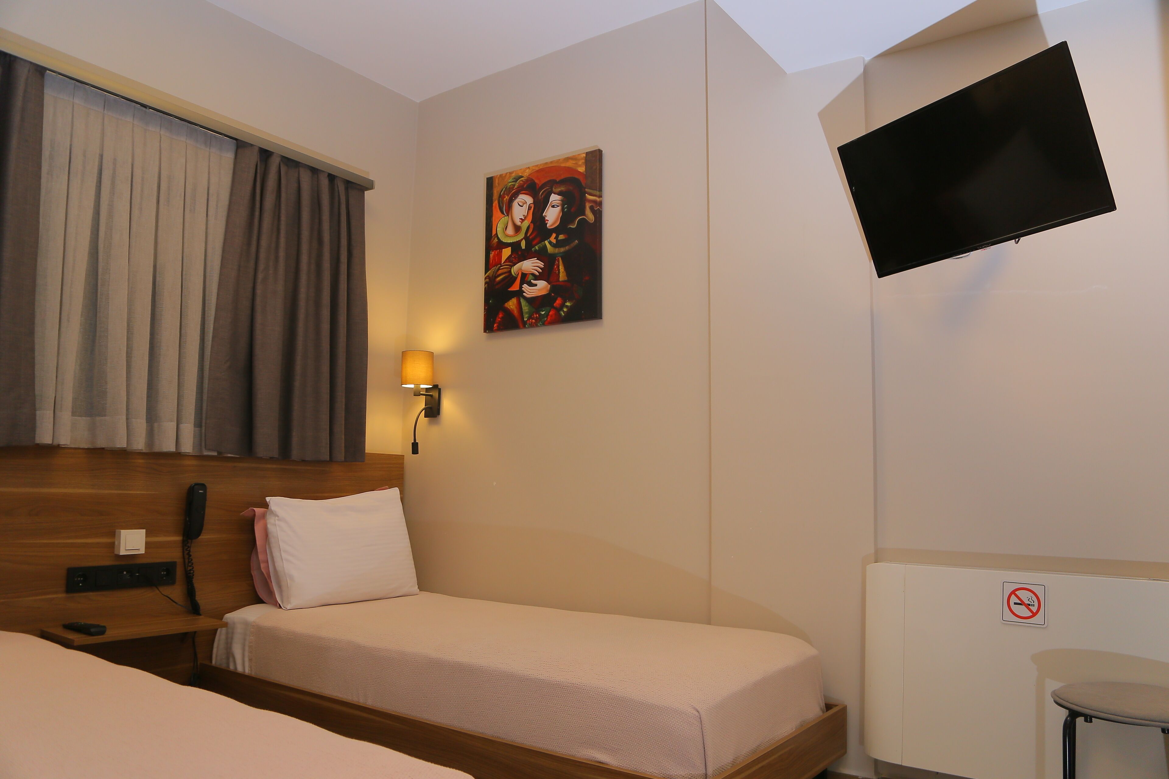 Una camera d'albergo con due letti, una TV fissata al muro, un comodino con una lampada e un quadro appeso al muro.