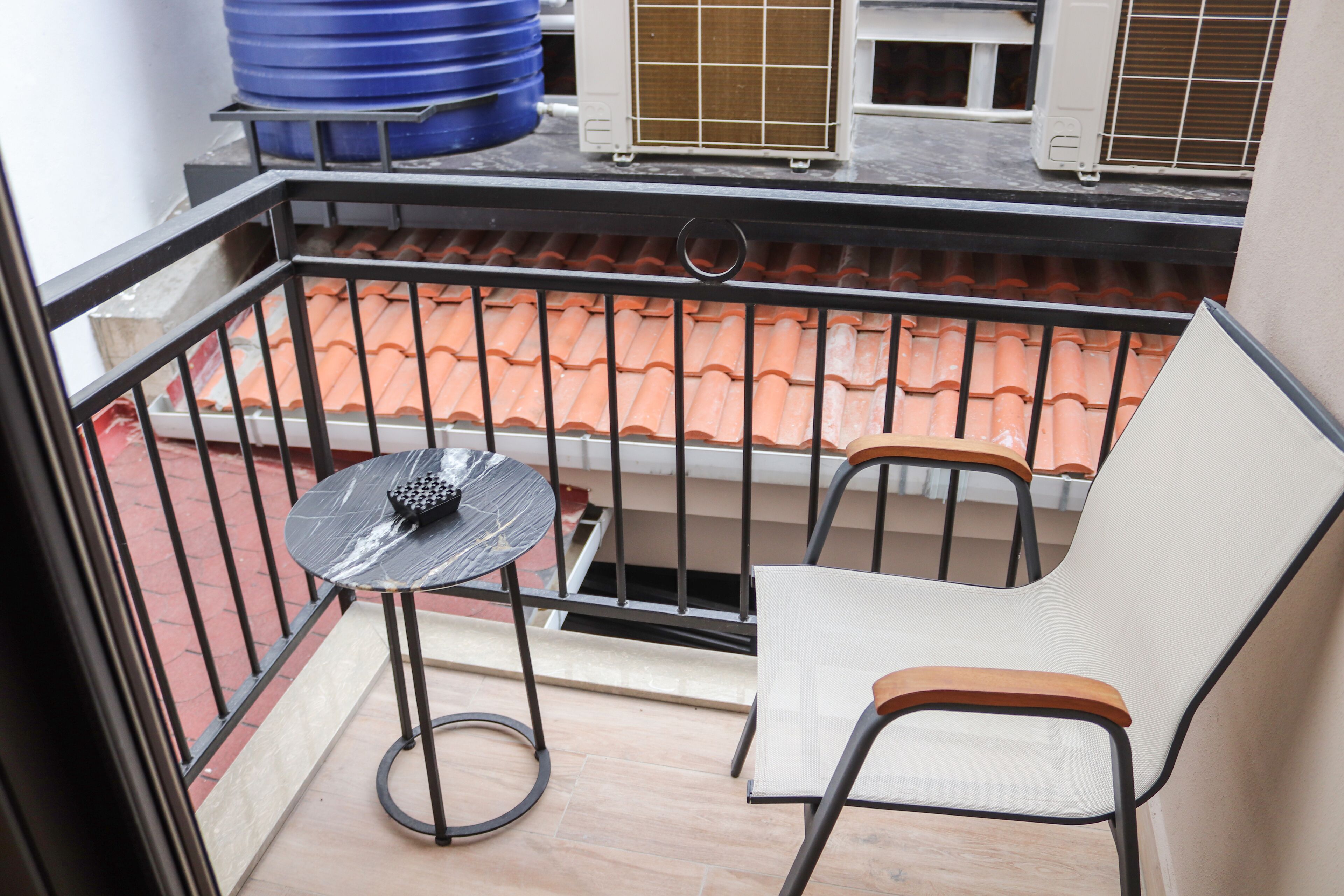 A balcony with a table and two chairs, a tiled roof, and a blue water tank in the background.