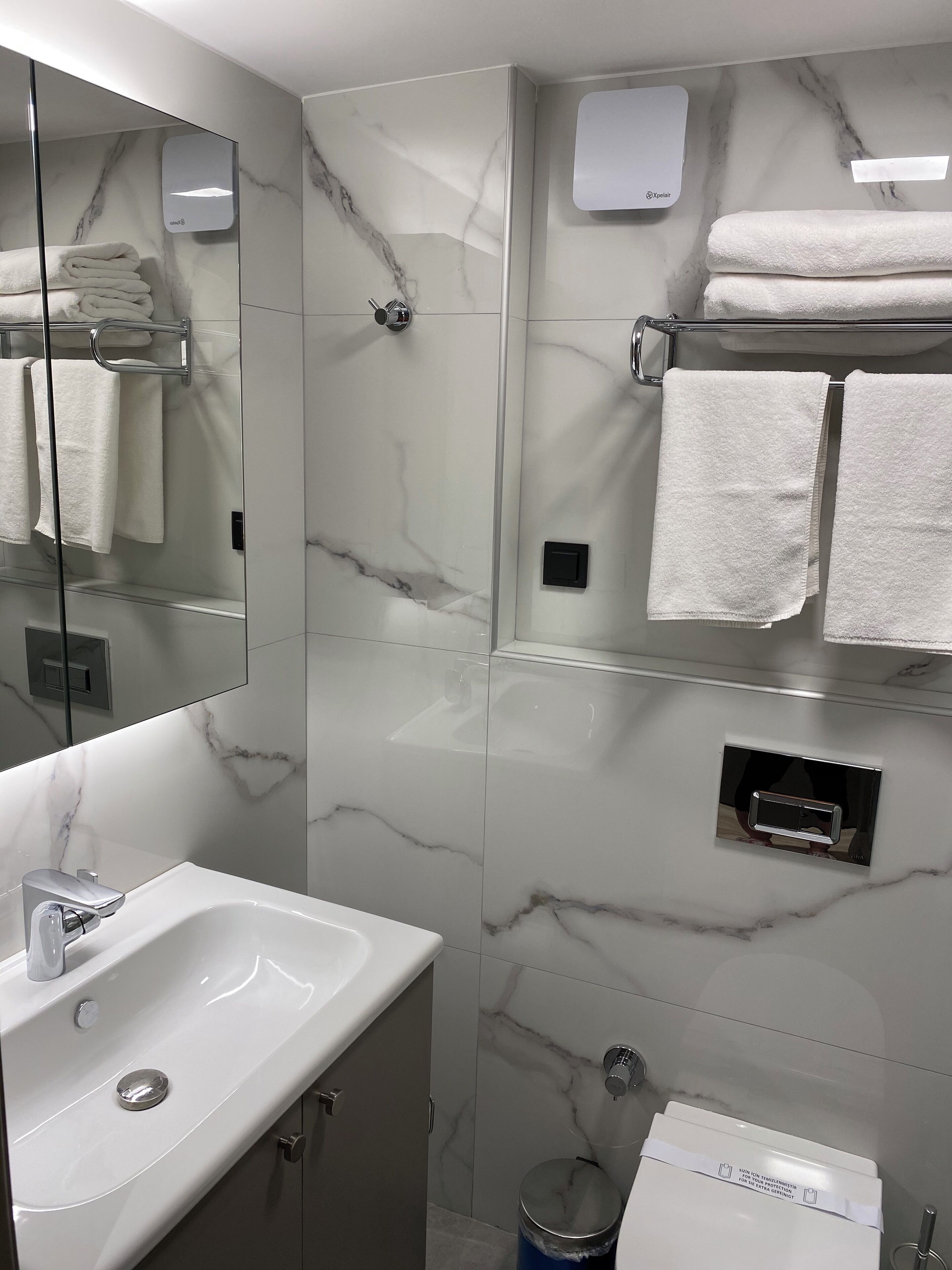 Ein modernes Badezimmer mit Marmorfliesen, einem Waschbecken mit Chromarmatur und einem Handtuchhalter mit gefalteten Handtüchern.