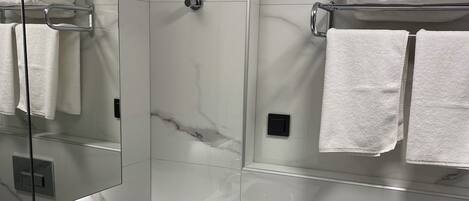 Ein modernes Badezimmer mit Marmorfliesen, einem Waschbecken mit Chromarmatur und einem Handtuchhalter mit gefalteten Handtüchern.