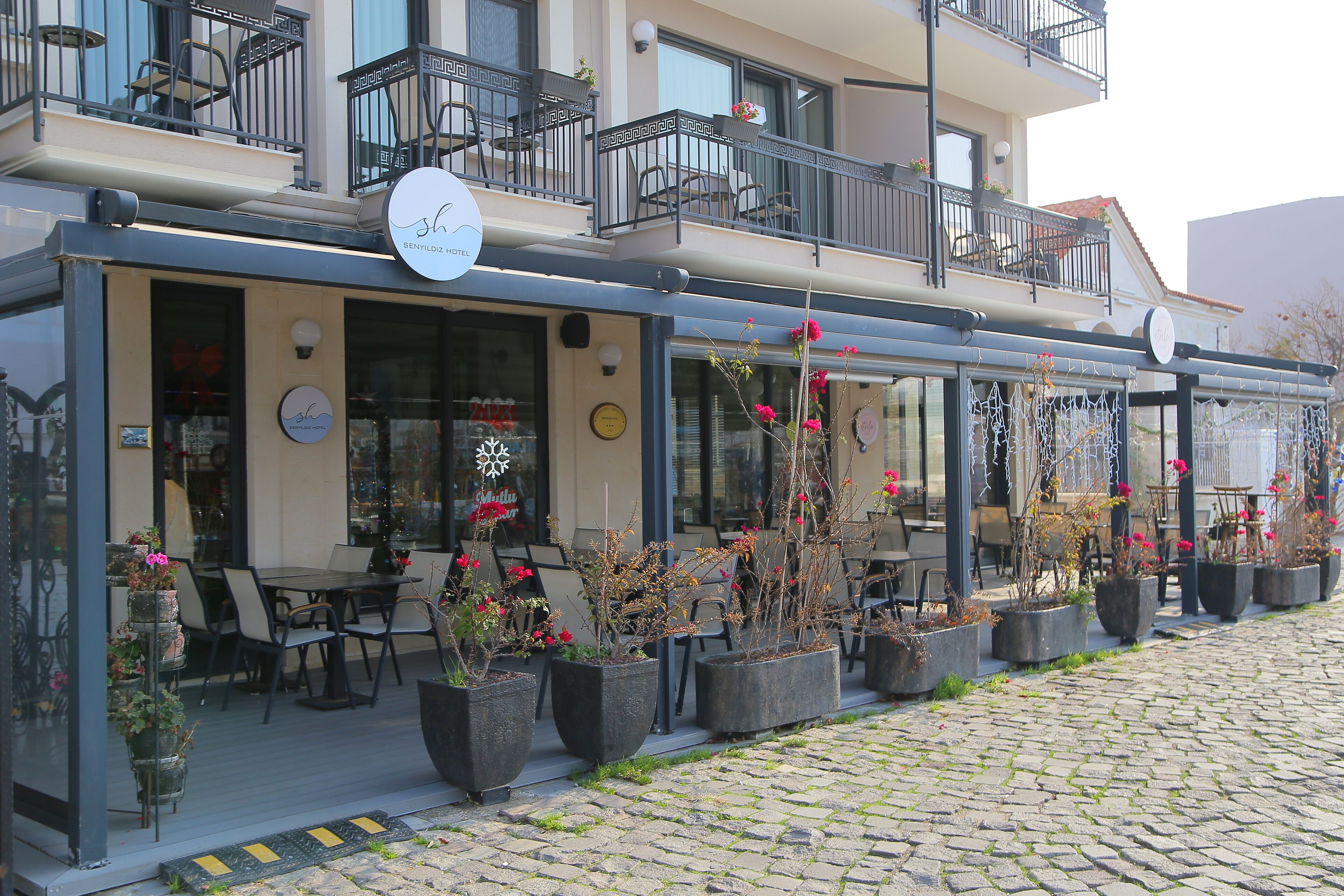 A hotel with outdoor seating, potted plants, and a balcony with chairs.