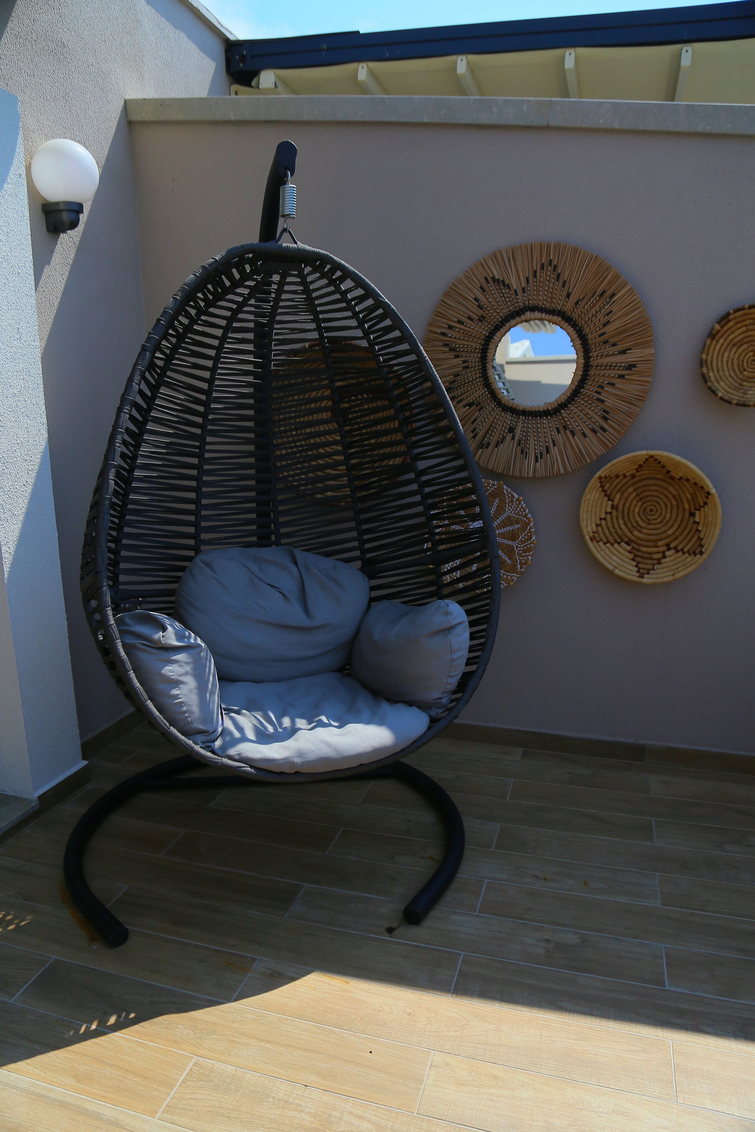 Un fauteuil suspendu en osier avec des coussins, un miroir fixé au mur et des assiettes décoratives en fibres tressées.