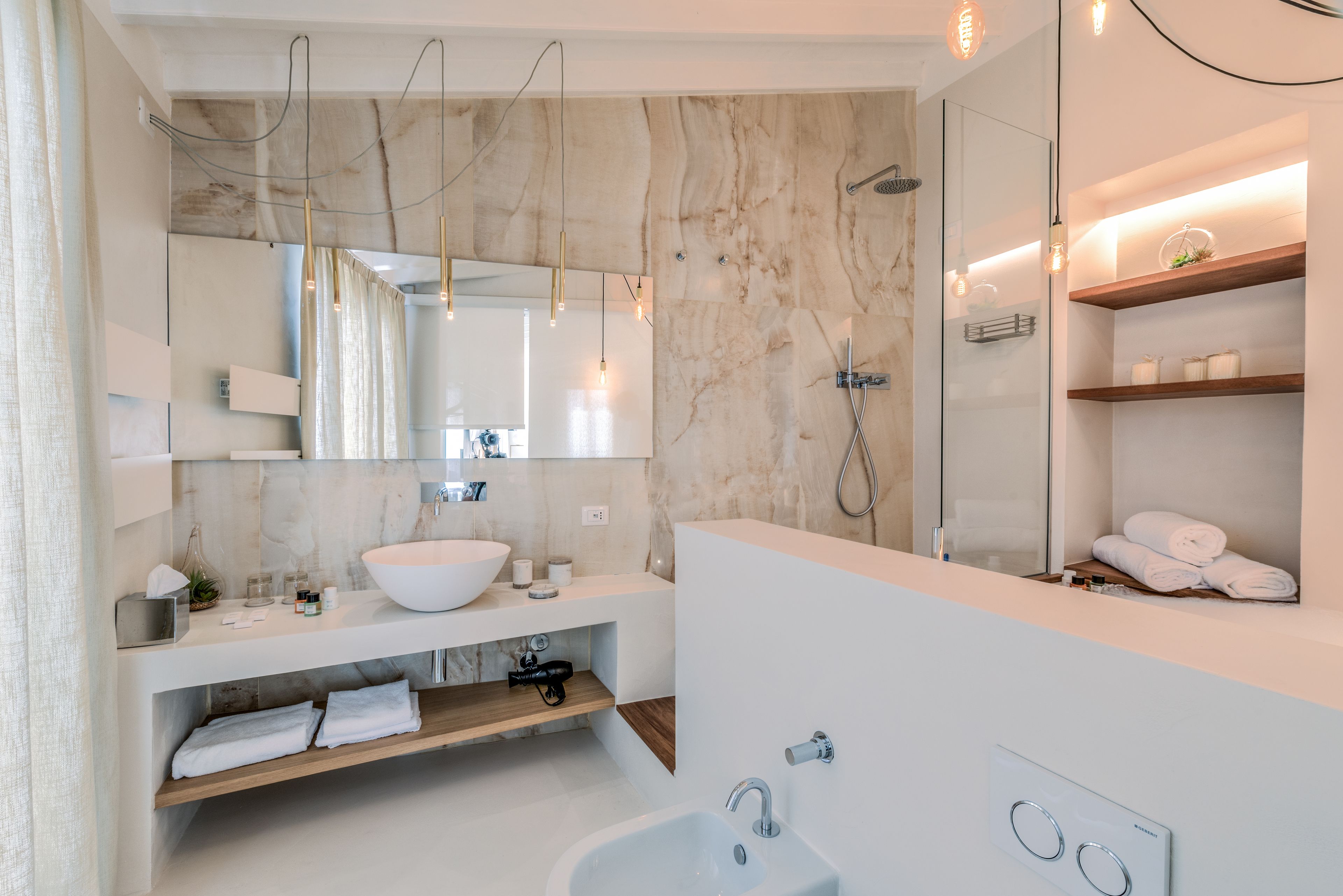 Un baño moderno con un lavamanos grande blanco, un espejo, una ducha y estantes empotrados con toallas.