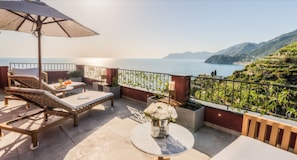 A terrace with lounge chairs, a table with flowers, and a view of the sea and hills. - Il Sogno di Manarola by The First (Riomaggiore)