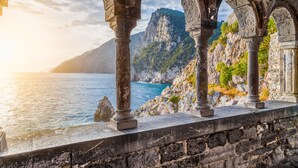 A stone structure with arches overlooking a coastal area with rocky cliffs and a body of water.