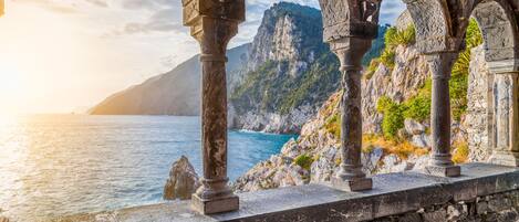 A stone structure with arches overlooking a coastal area with rocky cliffs and a body of water.