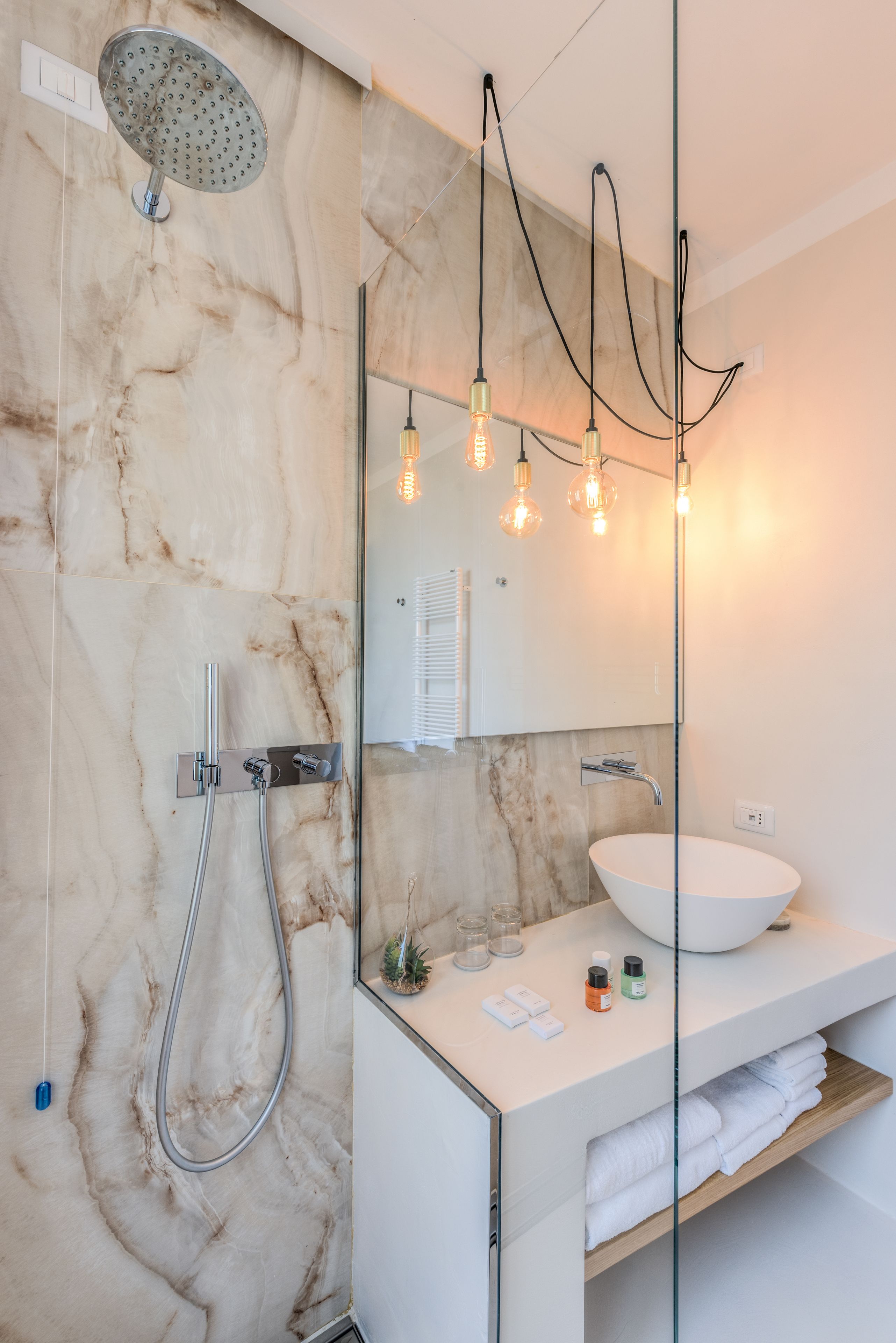 A modern bathroom with a marble wall, a freestanding shower, a round sink, and pendant lights.