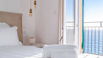 Habitación de hotel con cama, dos toallas, una lámpara de noche y vista al mar a través de una puerta de balcón.