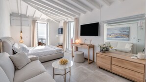 A modern, well-lit living room with a sofa, a round coffee table, a bed, a desk, and a TV.