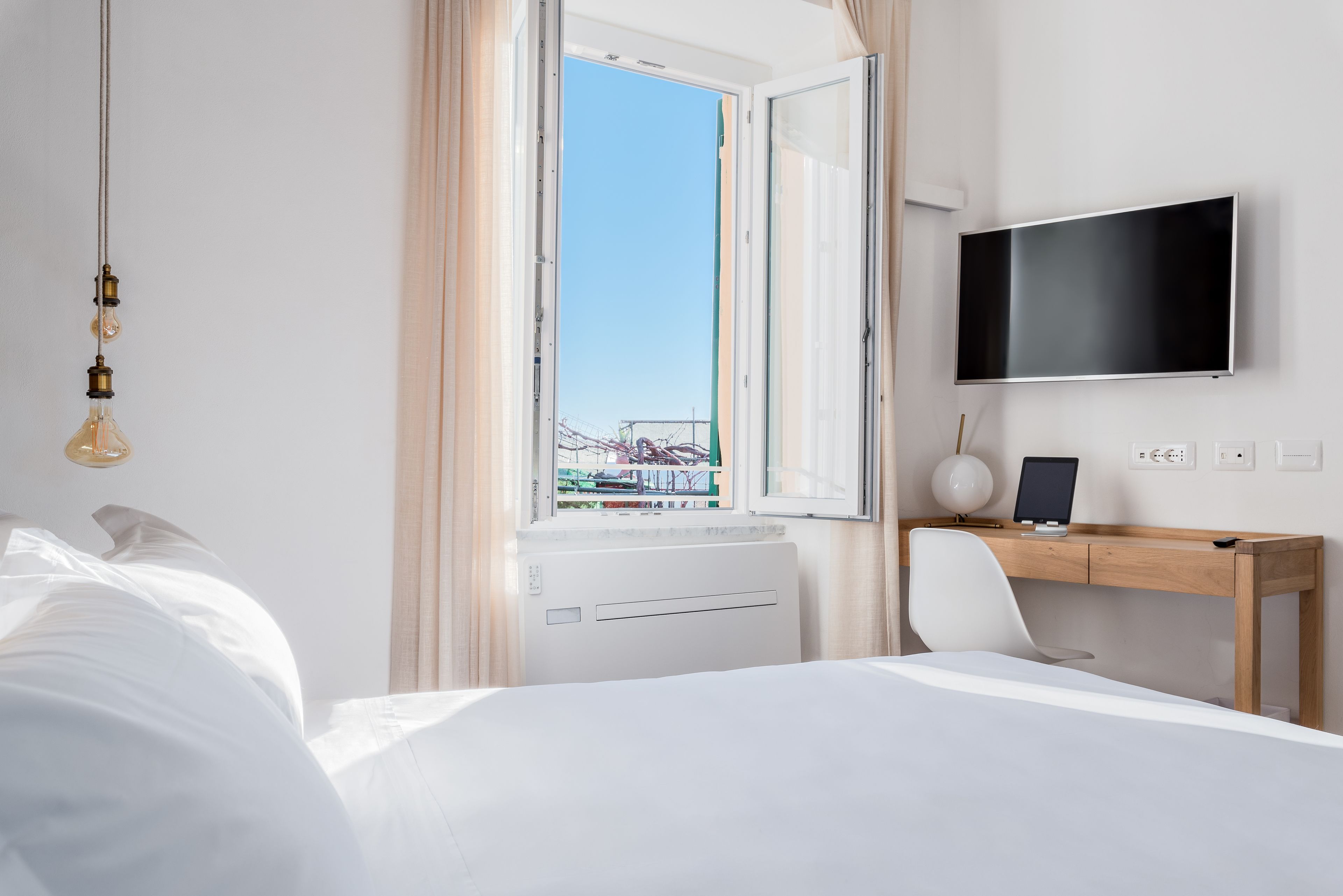 Une chambre d’hôtel comprenant un lit, un bureau, une chaise, une télévision et une fenêtre donnant sur un immeuble.
