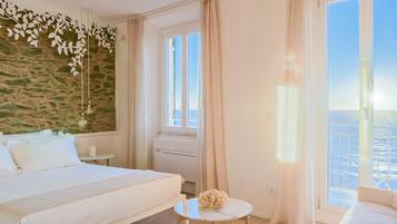 A hotel room with a bed, a small table, a decorative wall, a window with curtains, and a view of the city.