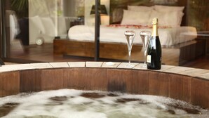 A hot tub with a bottle of champagne and two glasses. In the background, there is a bed with a wooden headboard and a nightstand with a lamp. - Villa Margaux (Fargues-Saint-Hilaire)