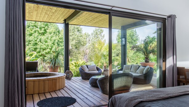 A modern bedroom with a large bed, a wooden deck, and a hot tub. - Villa Margaux (Fargues-Saint-Hilaire)