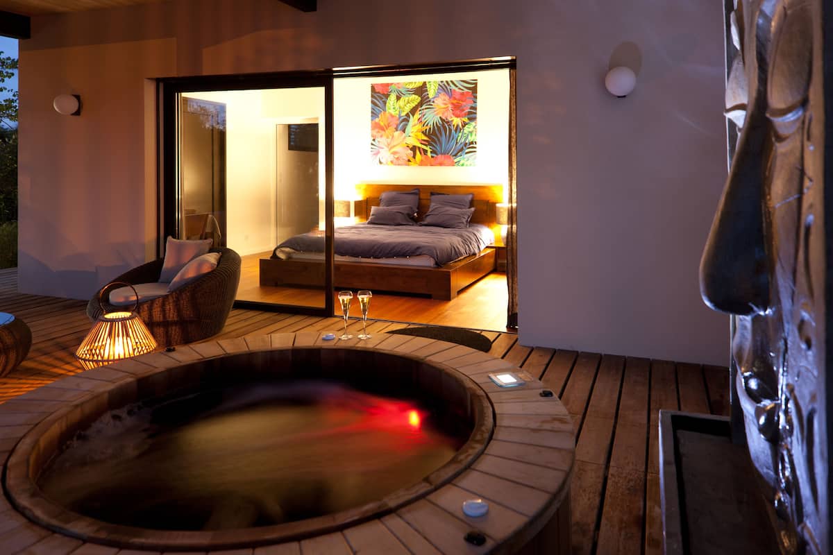 A modern bedroom with a large bed, a hot tub, and a wicker chair.