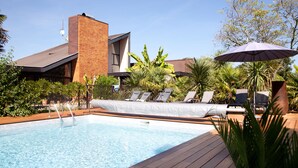 A pool area with a modern building, lounge chairs, and a large umbrella. - Villa Margaux (Fargues-Saint-Hilaire)
