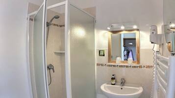 A bathroom with a glass-enclosed shower, a sink, a mirror, and a hairdryer.